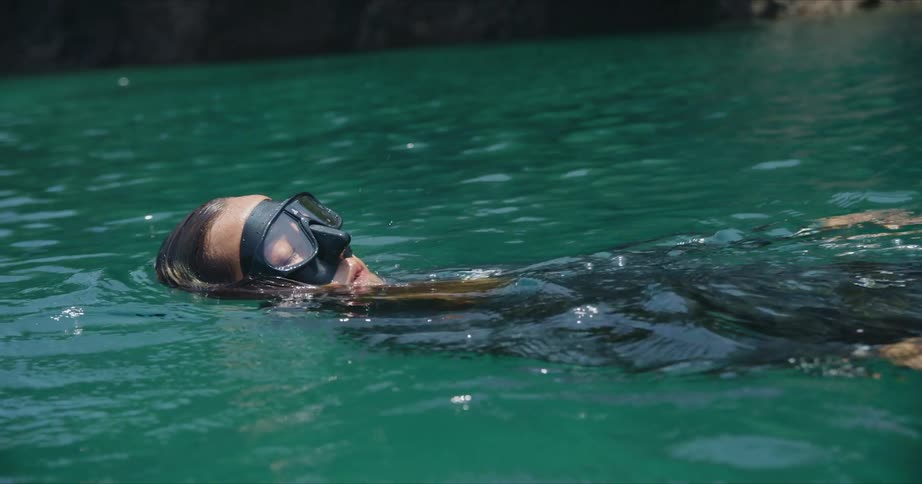 A woman wearing swimming goggles and a wetsuit is in the water swimming on her back