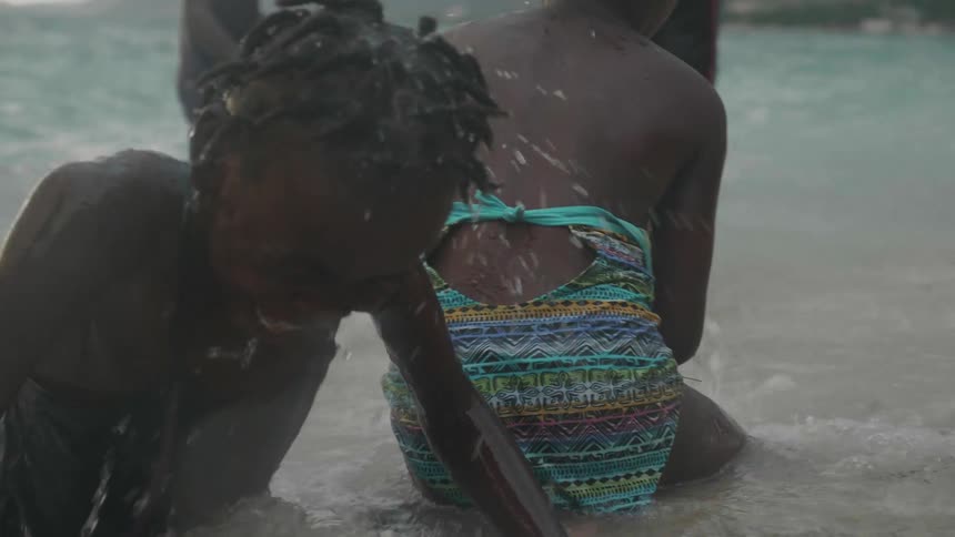 A group of children with dreadlocks swimsuit and shorts plays on the beach at bay