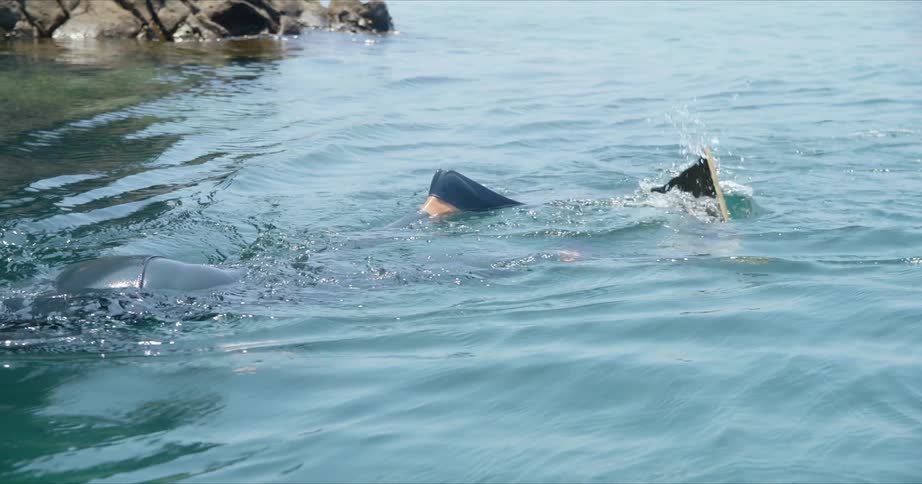 A diver kicks their swimming fins above the water while passing a cave