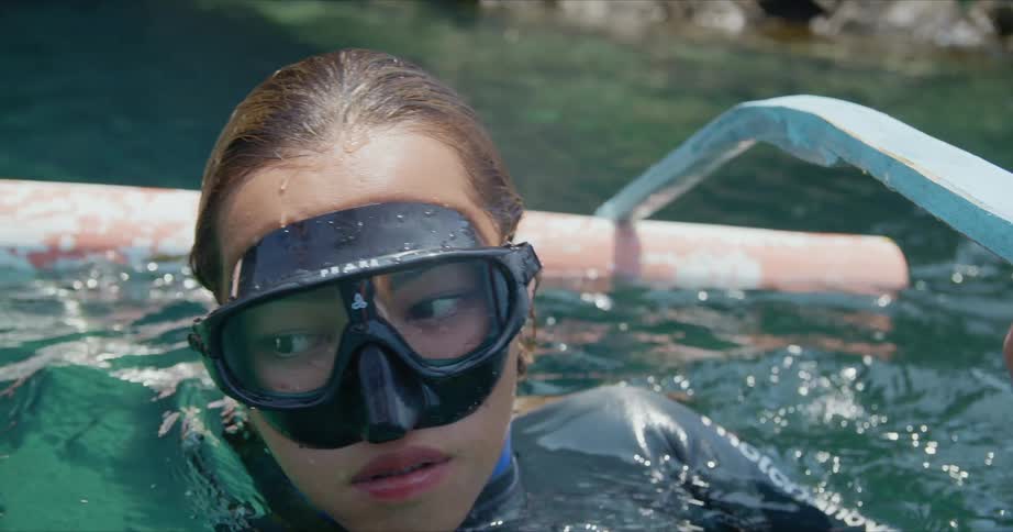 A woman wearing swimming goggles and a wetsuit is in the water looking around