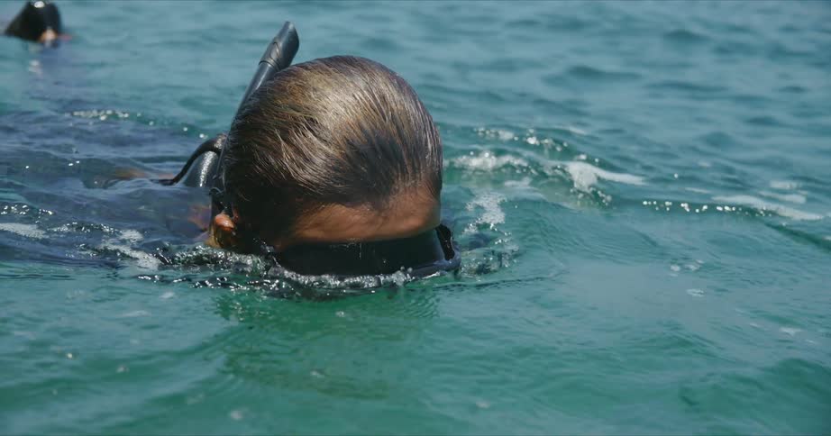 A woman wearing a wetsuit is snorkeling on the surface of ocean water