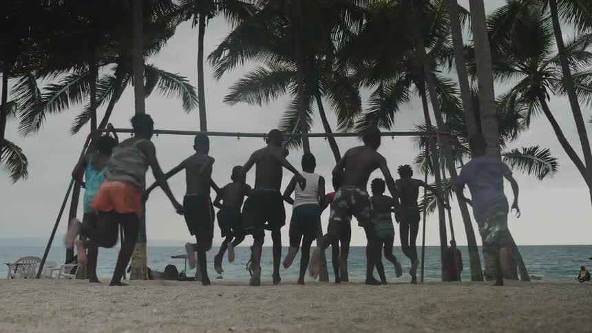 Boys and girls running on a beach with trees with the ocean sky and clouds in the background