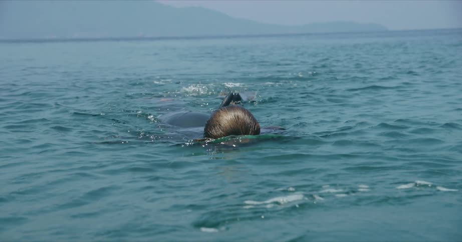 A swimmer is snorkeling with their face in the water and diving fins on their feet