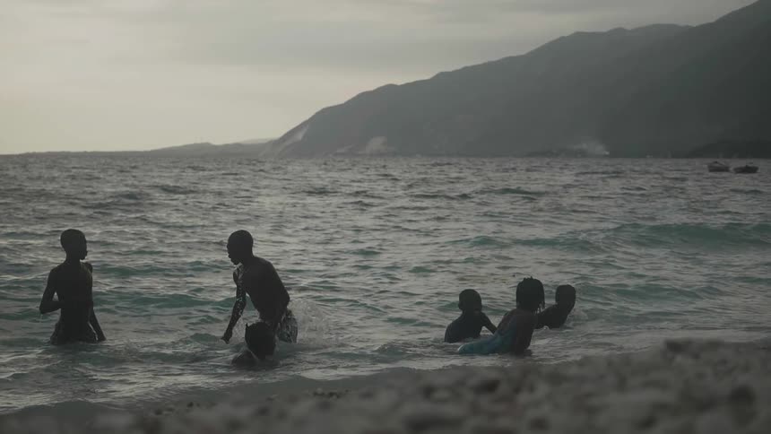 Boys and girls in the water on the beach with the sky and clouds in the background