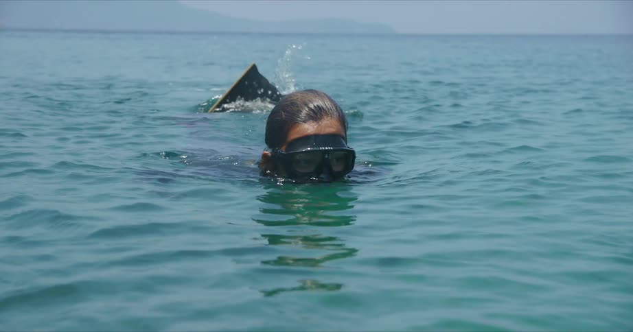 A person is swimming on the ocean surface wearing scuba gear in the daytime