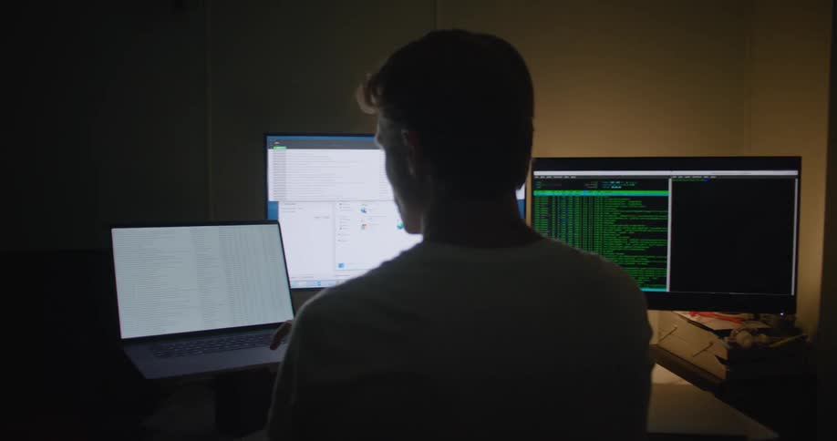 A man is sitting at a desk in front of 3 computer screens