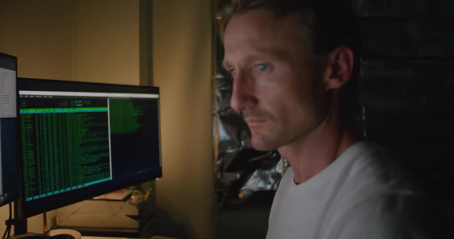 A man is working at a computer workstation while at home at dusk