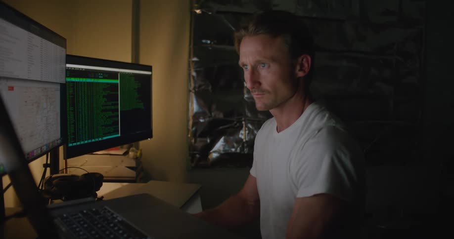 A man in an enclosed room using a multi monitor computer