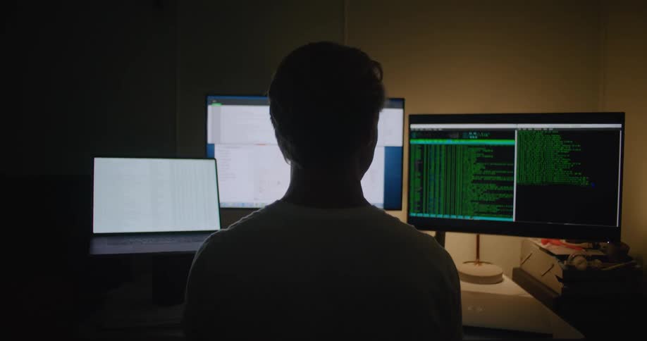 A man is looking at computer monitors in the dark
