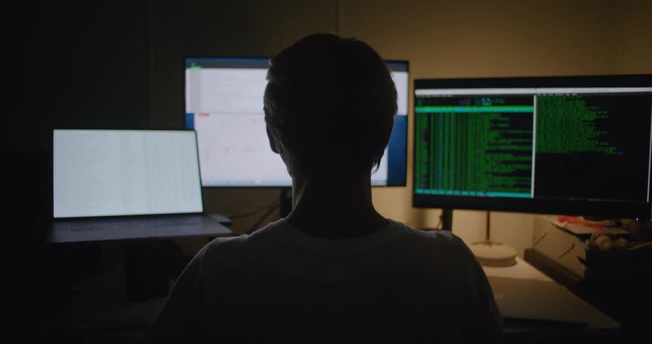 A man is sitting at computer workstation at home waiting while the computer processes information at night
