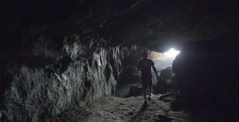 A man walks out of a cave towards the sunlight