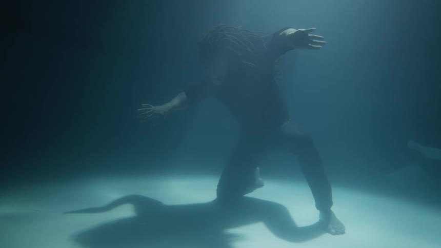 A man kneels at the bottom of a pool and moves his arms in dance poses