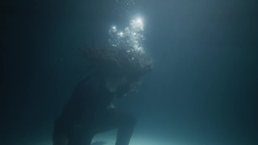 Sad and angry man with braided hair beard and black shirt screams underwater