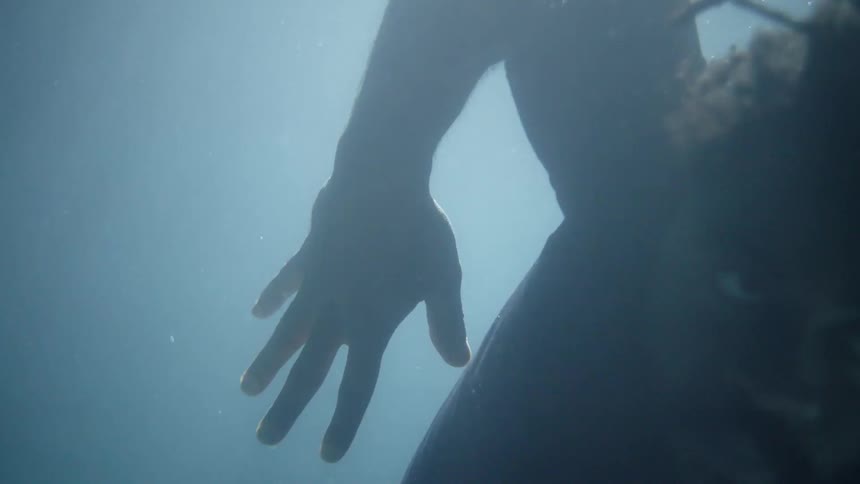 A man is underwater with his eyes open and moving his arms in a swaying motion