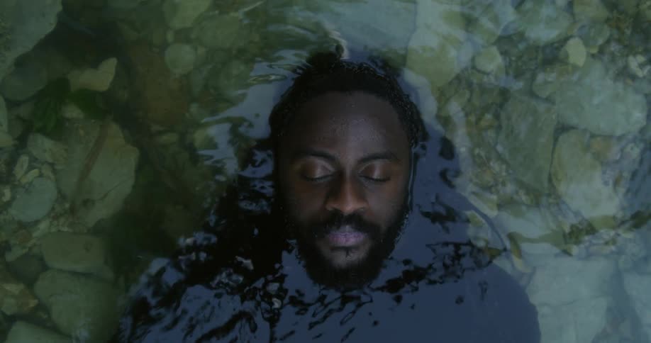 Man with beard and long hair lies on his back in stream water