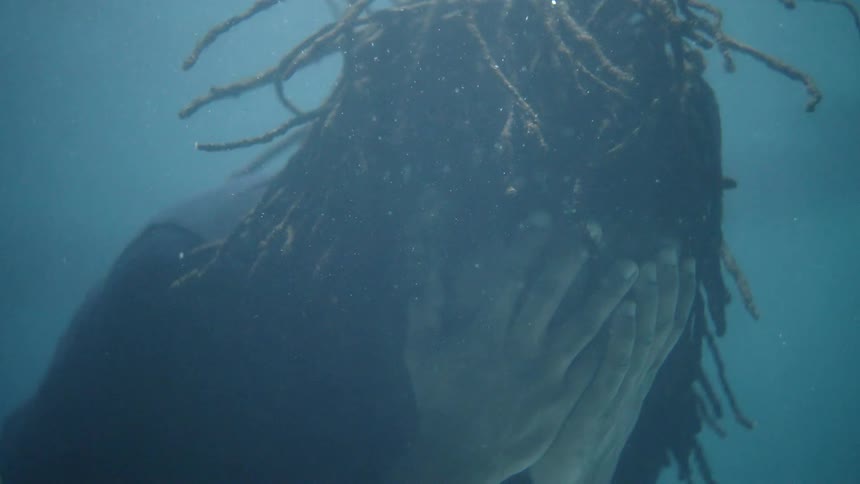 A man covers his face with his hands while floating underwater in a pool