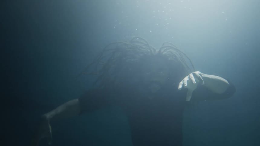 A man with dreadlocks is floating underwater performing modern dance movements