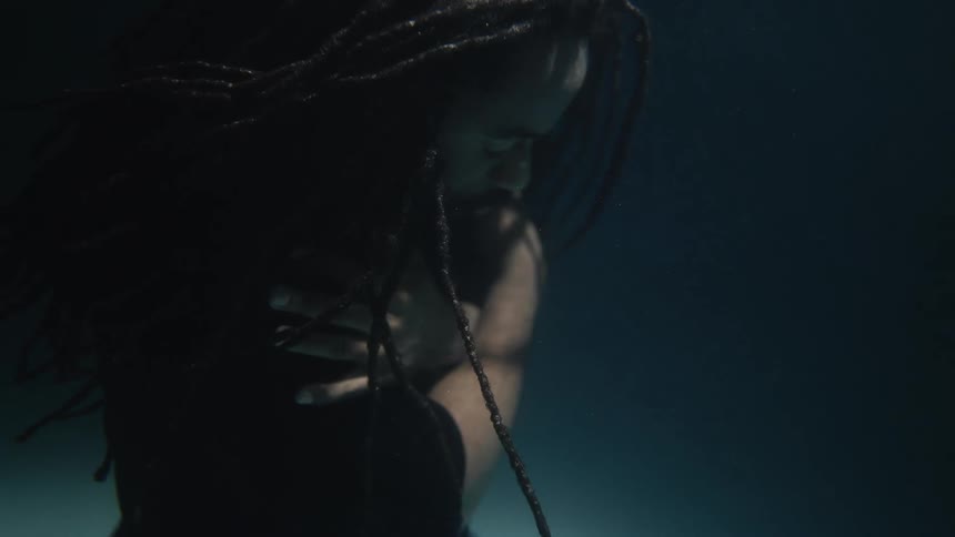 A man is floating underwater with his arms folded