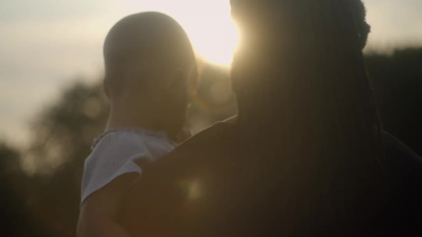 Father with braided hair holds son and walks in the forest at sunset