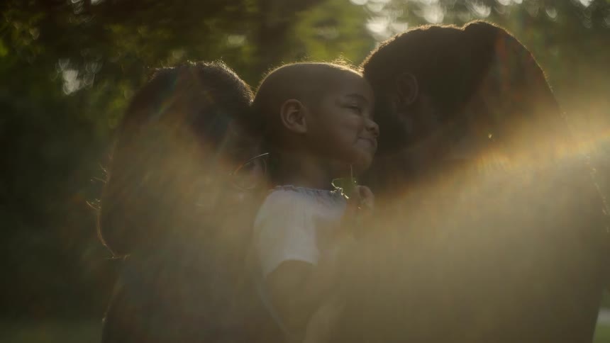 A mom and dad embrace their little girl holding her between them in the glare of the sunshine