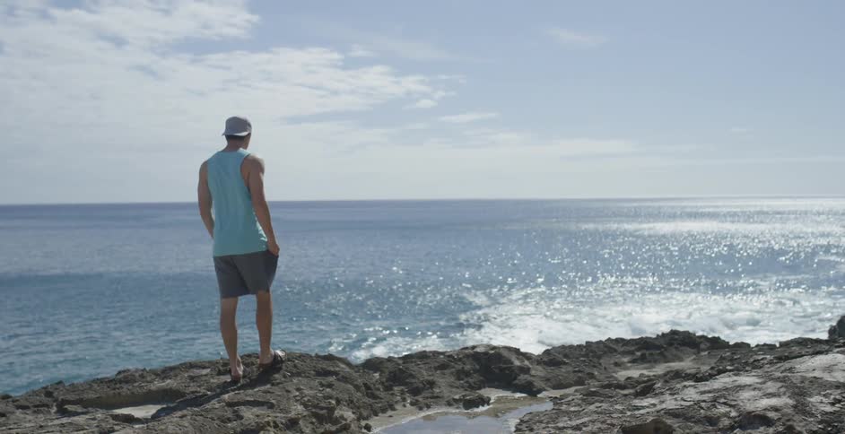 A man walks over rocks towards the water