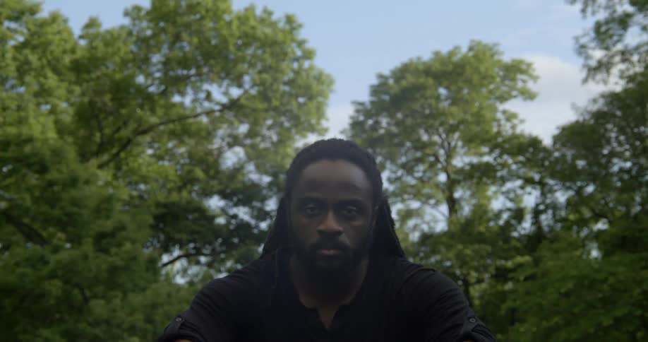 A black man opens his eyes and looks ahead with trees in the distance