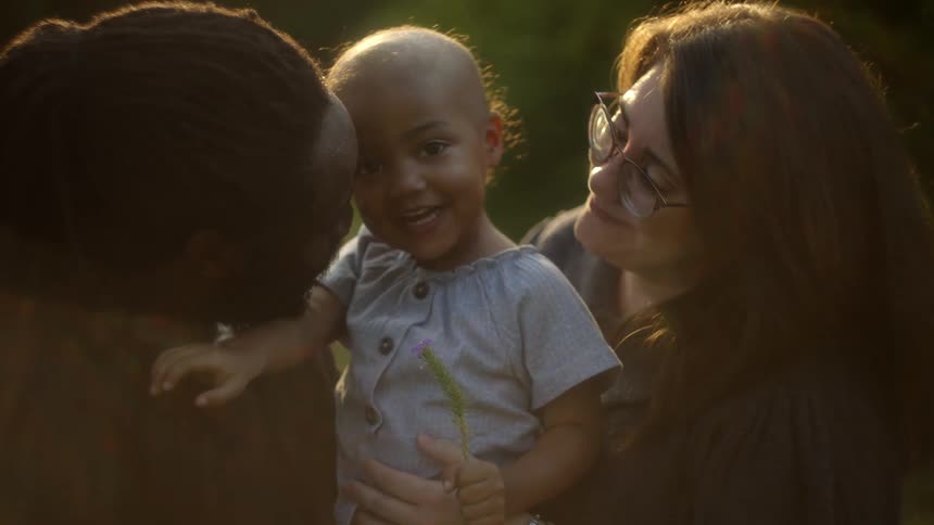 A little girl smiles and laughs while being held between her mom and dad