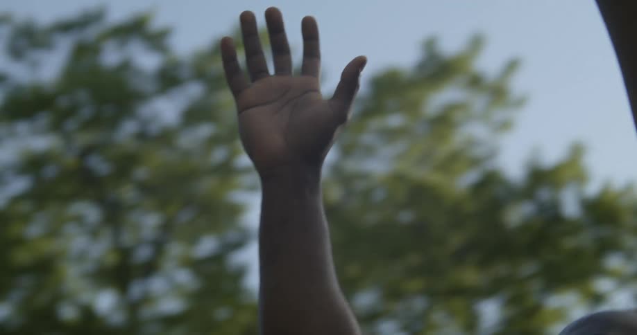 A black man is raising his hands high in the air as sunlight shines upon him