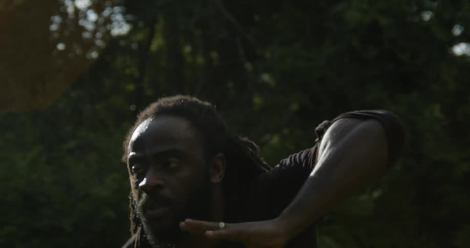 A man is performing a modern dance outdoors in a wooded area during the daytime