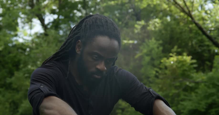 A man sits with his arms resting on his knees in a park