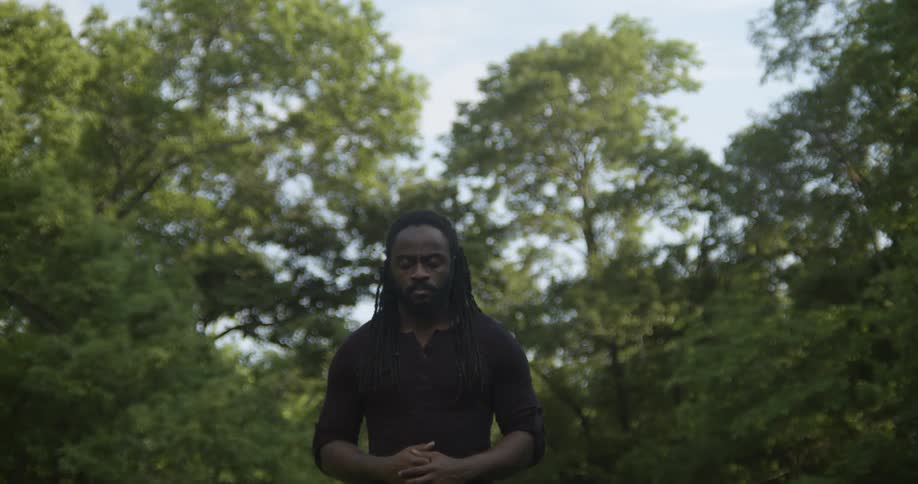 A man closes his eyes and bows his head while meditating in a park