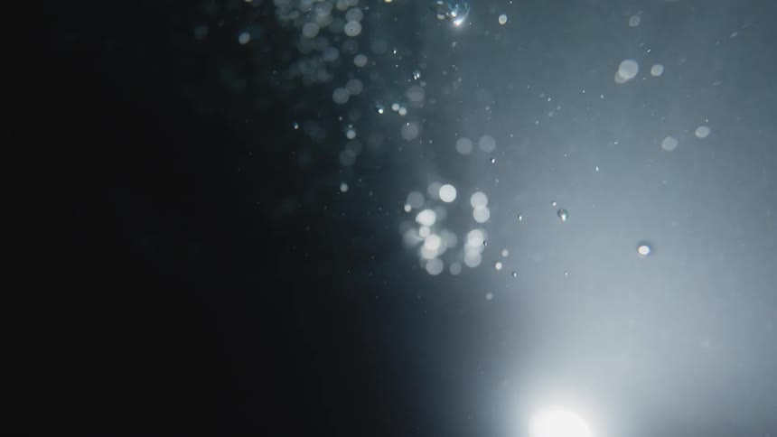 Bubbles rise through dark water toward bright light shining against blackness