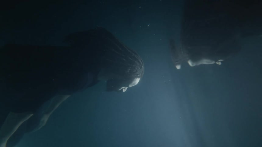 A man laying on the bottom of a dark and shadowy pool gets up and floats to the surface
