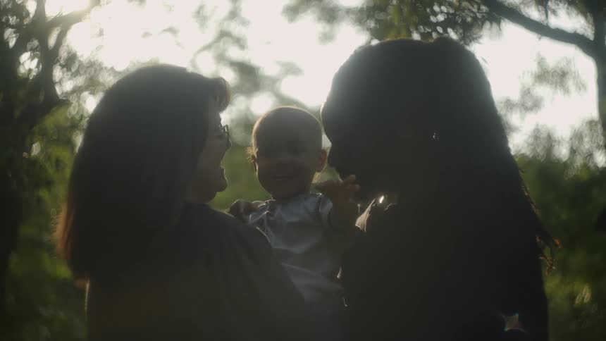Man with long hair and beard and woman with glasses brown hair hold baby toddler in the forest