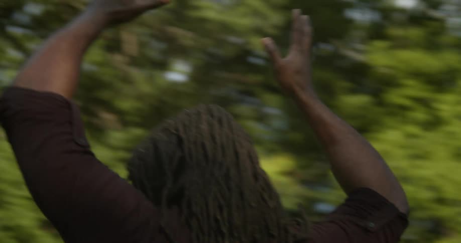 A man throws his arms in the air as he dances with his eyes closed in a park