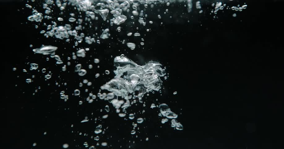 Bubbles slowly rise in the dark water
