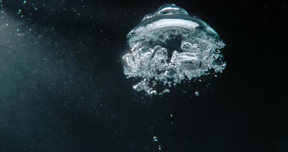 A plume of bubbles is rising underwater with light rays providing the only illumination