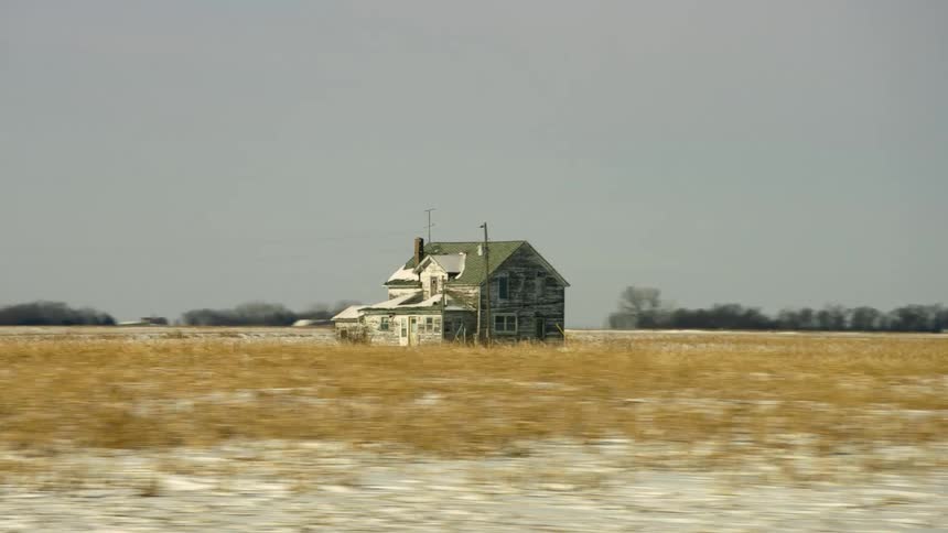 A house in the middle of a field with trees the sky and clouds in the background