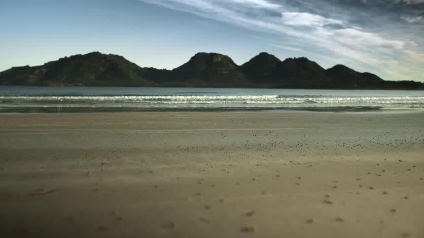 Waves roll onto a beach with mountains in the distance
