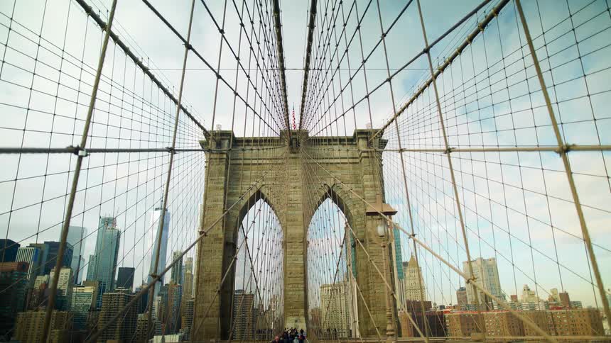 A view of the arch of a suspension bridge and city buildings are in the distance