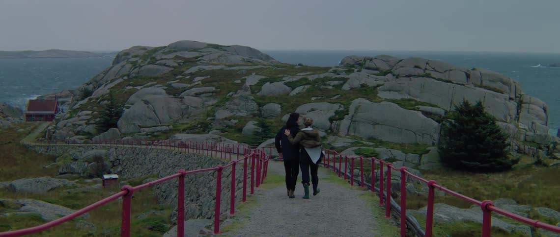 A couple hug as they walk on a trail toward the coast