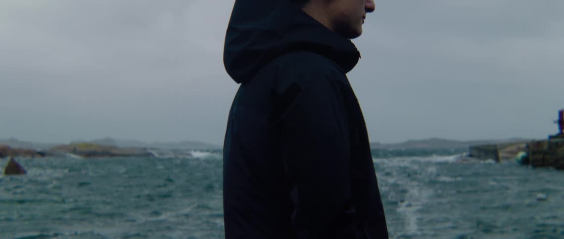 A man stands and watches the ocean as heavy wind causes ripples and waves in the water