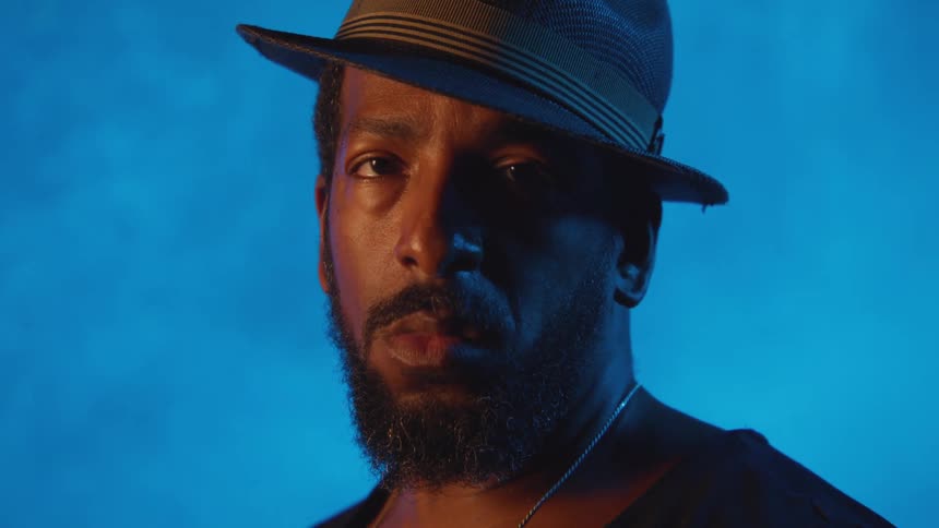 A man wearing a hat looks up with blue smoke background