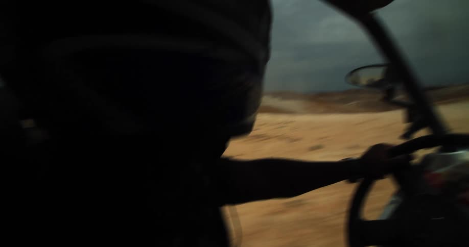 A person with a helmet driving a vehicle in a desert with the sky and clouds in the background