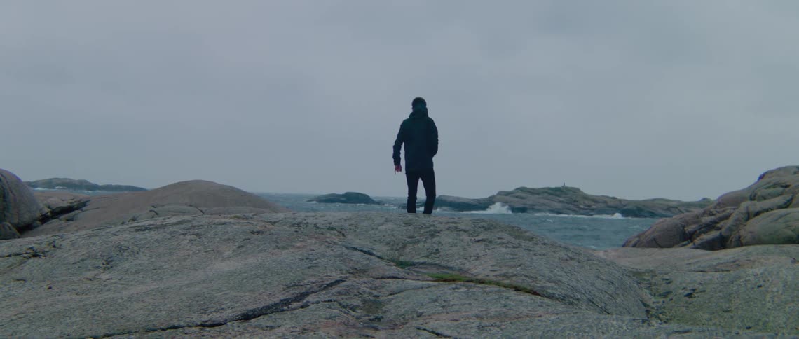 A man wearing dark clothes is walking on the rocks along a seashore
