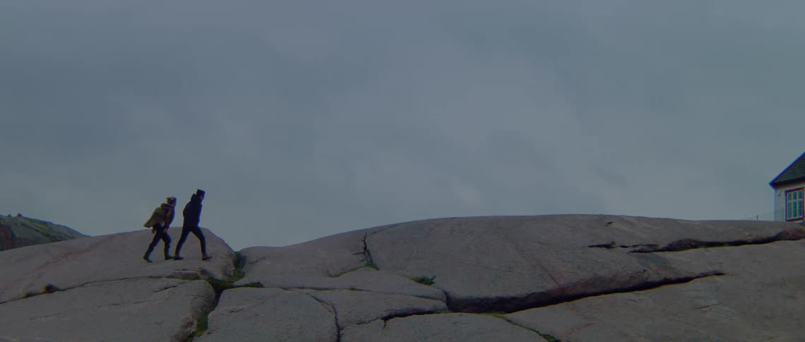 Two people are walking across rocks towards a building