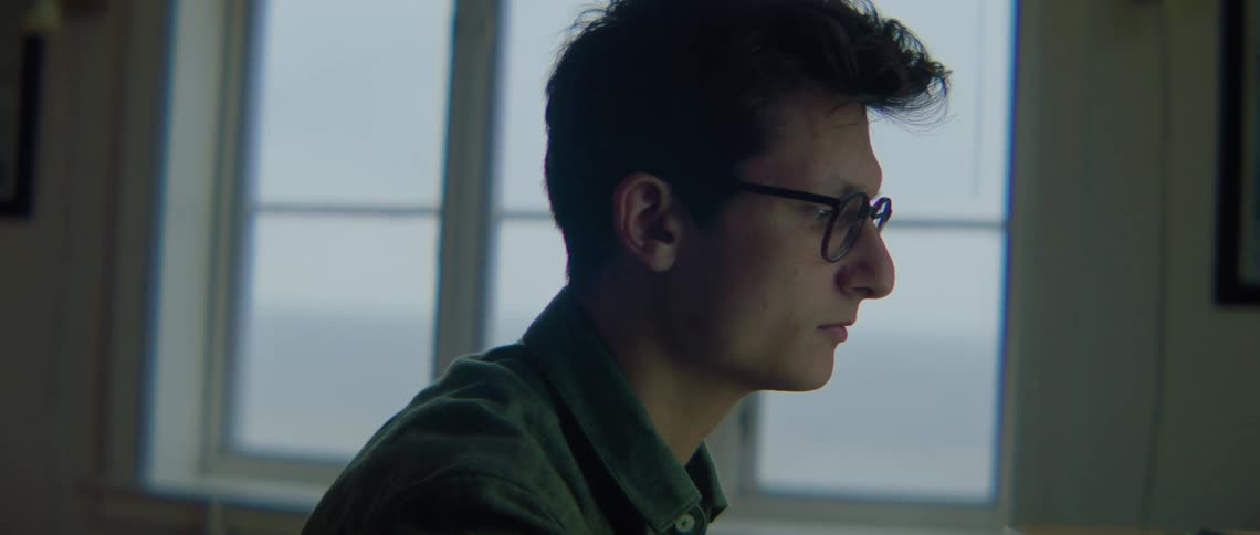 Man with glasses and green shirt sitting at desk uses computer in room