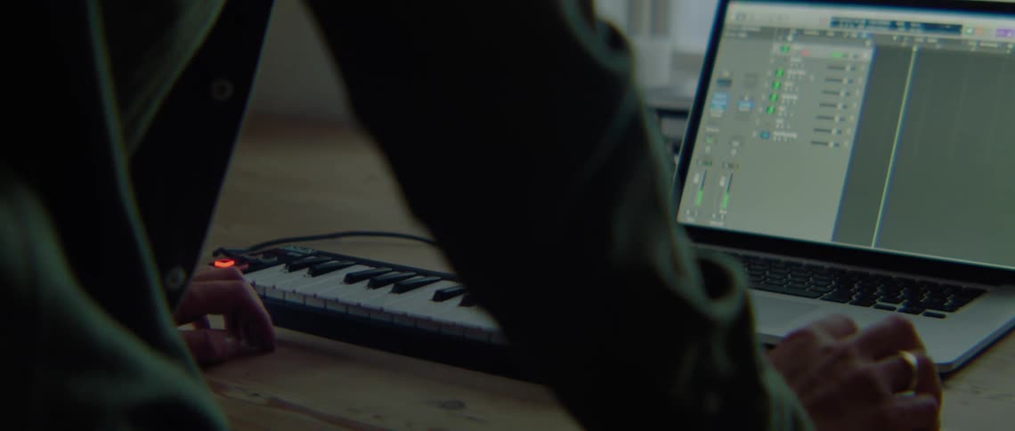 Man with green shirt records from digital piano to laptop in room