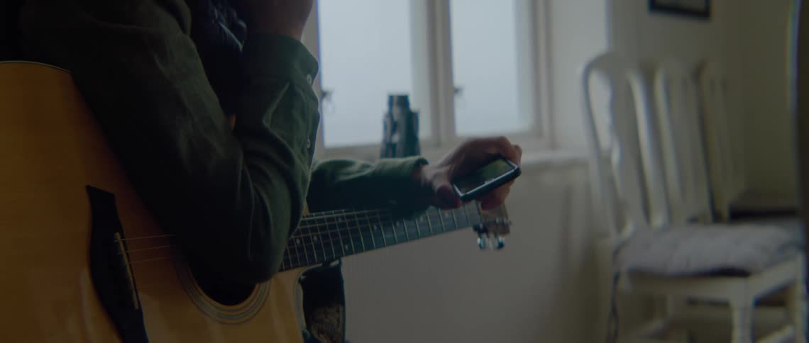 A man holds a guitar under his arm while looking at his smartphone