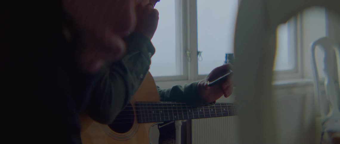 A man with glasses and a guitar looking at a smart phone with a woman next to him